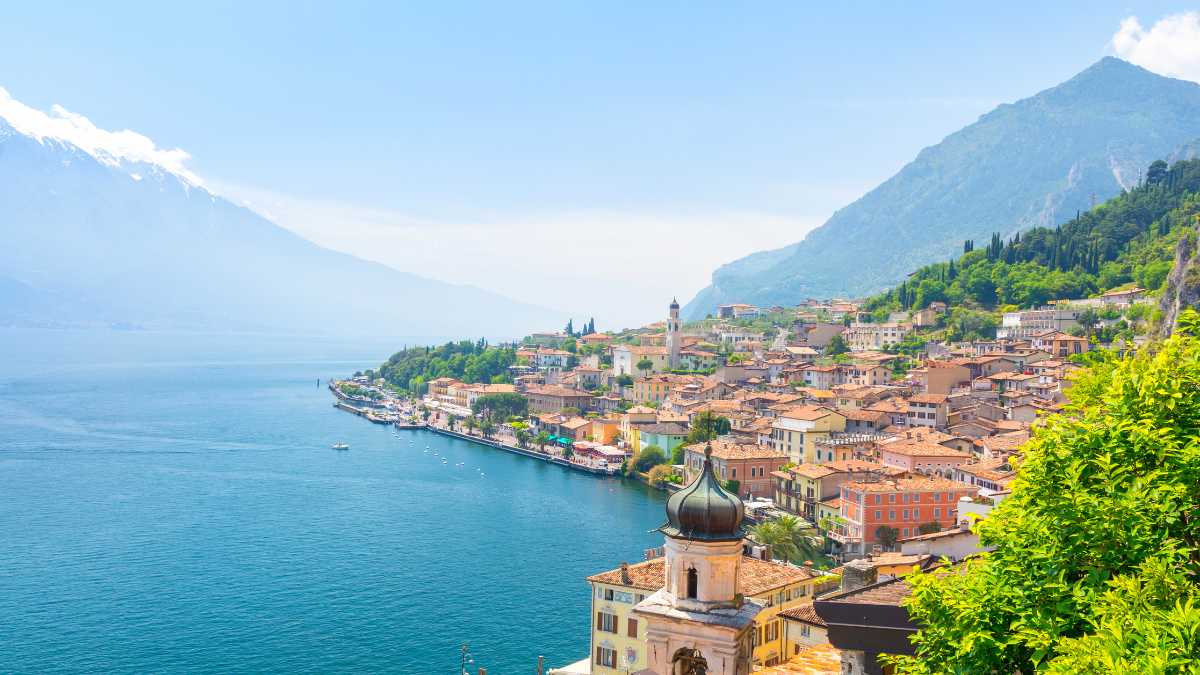 Dettaglio di una spiaggia di ciottoli a Limone sul Garda, con acqua trasparente, gente che si rilassa e qualche sport acquatico in corso